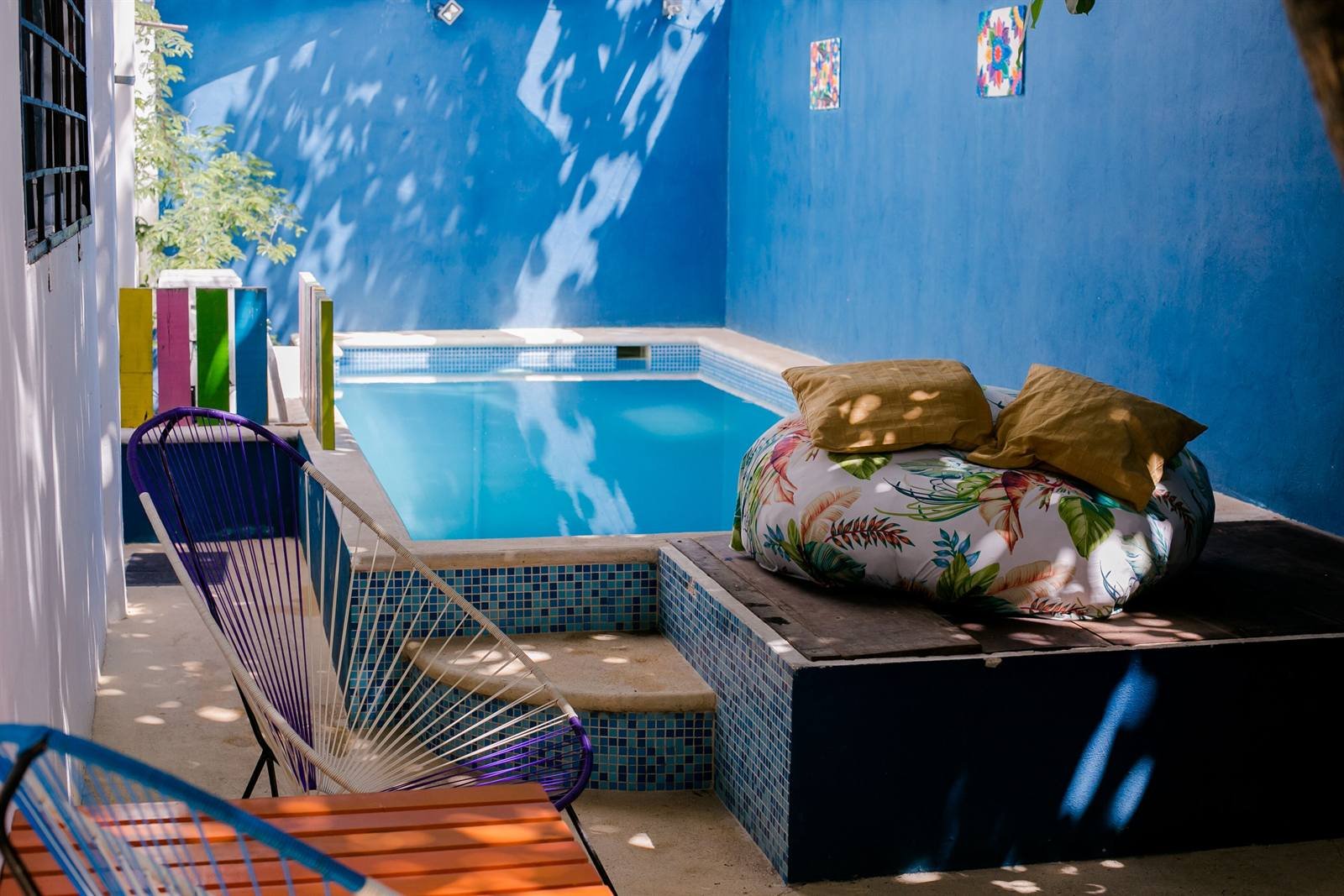 Small plunge pool with blue walls, woven chairs and a big floor cushion