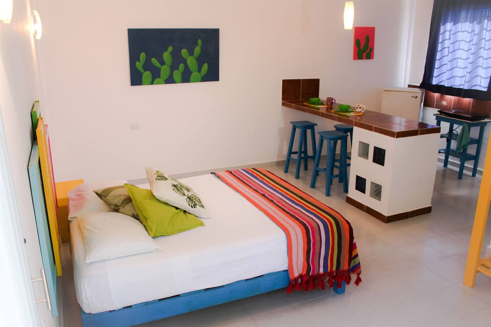 Room with a striped blanket, desk with stools and kitchenette